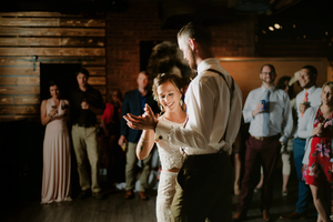 Couple dancing together at a rustic wedding reception with guests watching in the background.