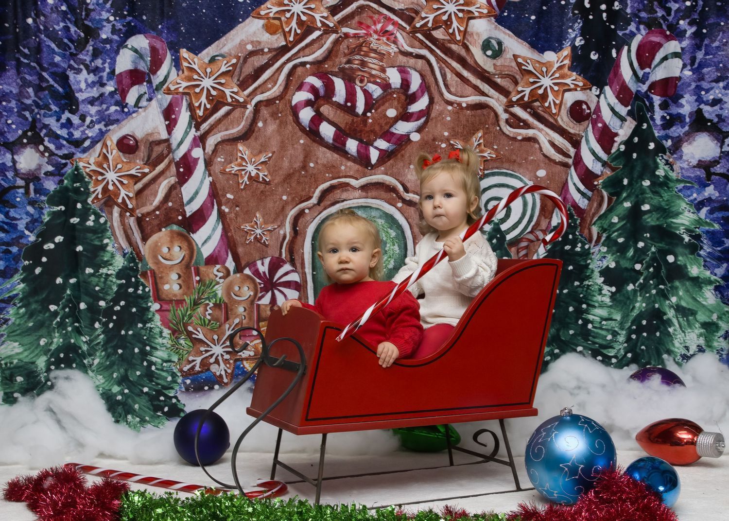 A festive holiday scene with a red sleigh against a gingerbread house backdrop with Christmas ornaments.