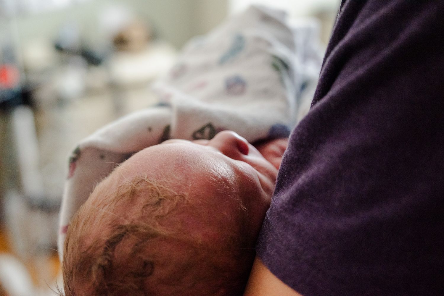 Newborn baby with dark hair being cradled in parent's arms in hospital room.