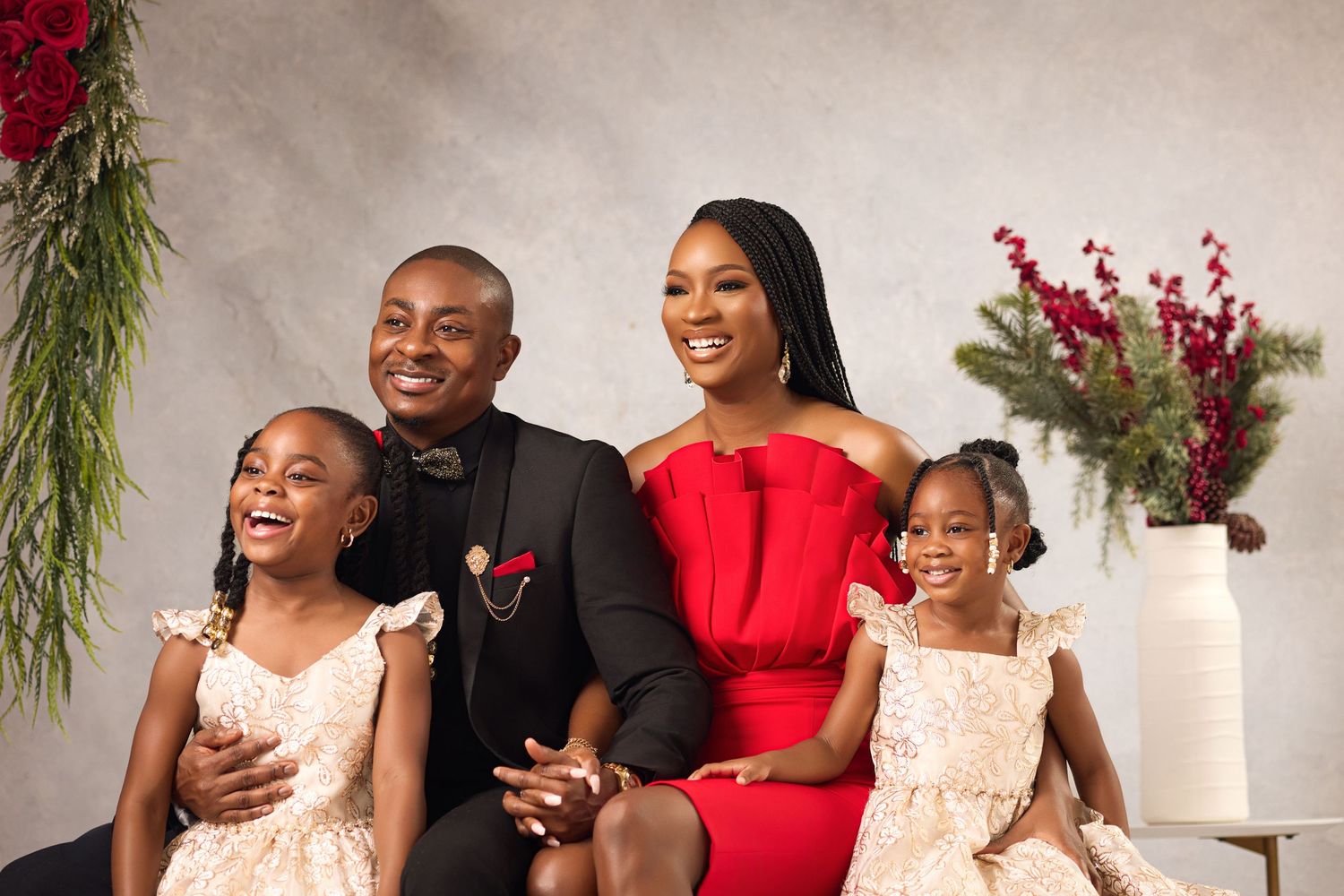 Family portrait with formal attire against a neutral backdrop with red floral decorations.