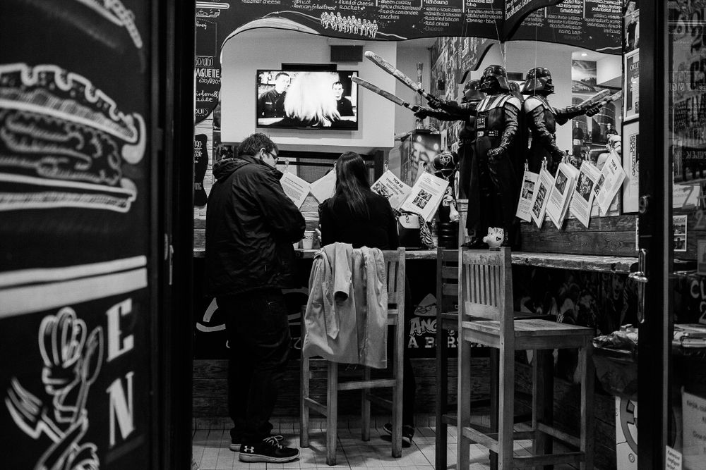Interior of a casual dining establishment with customers seated at tables and a TV mounted on the wall.