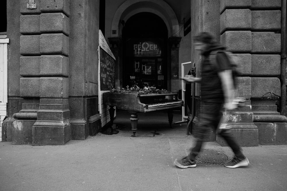 Motion blur of pedestrian walking past ornate stone archway in urban setting.
