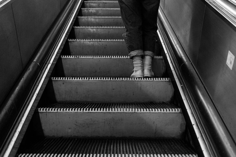 Close-up view of feet on an ascending escalator in a monochromatic urban setting.