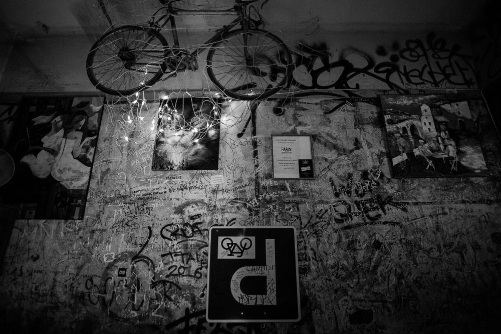 Urban wall covered in graffiti with a bicycle hanging overhead in a dimly lit space.