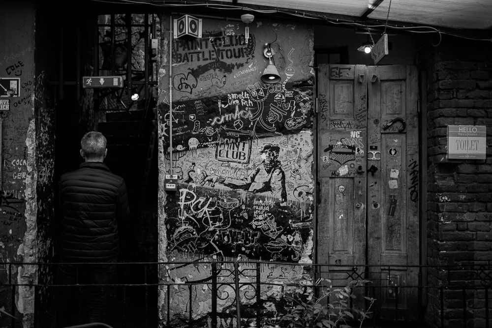 Grungy wall covered in street art and posters with wooden doors in low light.