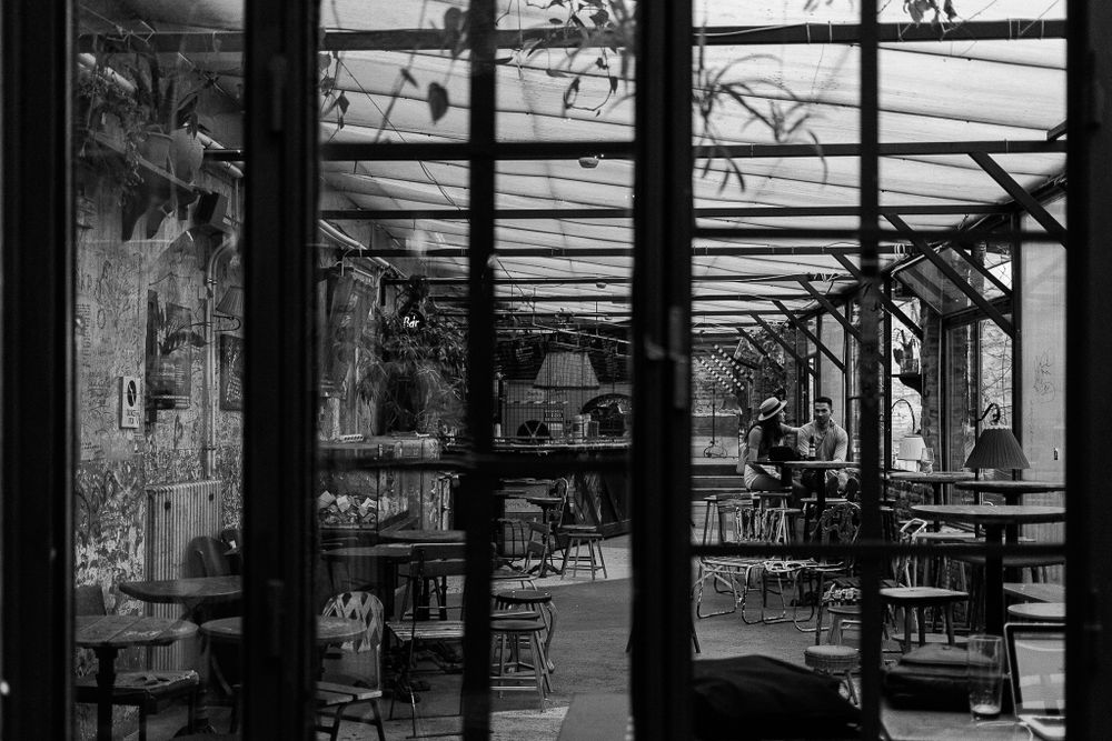 Empty restaurant interior viewed through window panes with industrial ceiling beams visible.
