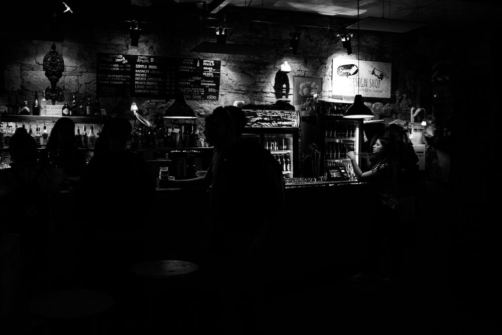 Dramatic black and white nighttime urban scene with silhouetted figures and glowing lights.