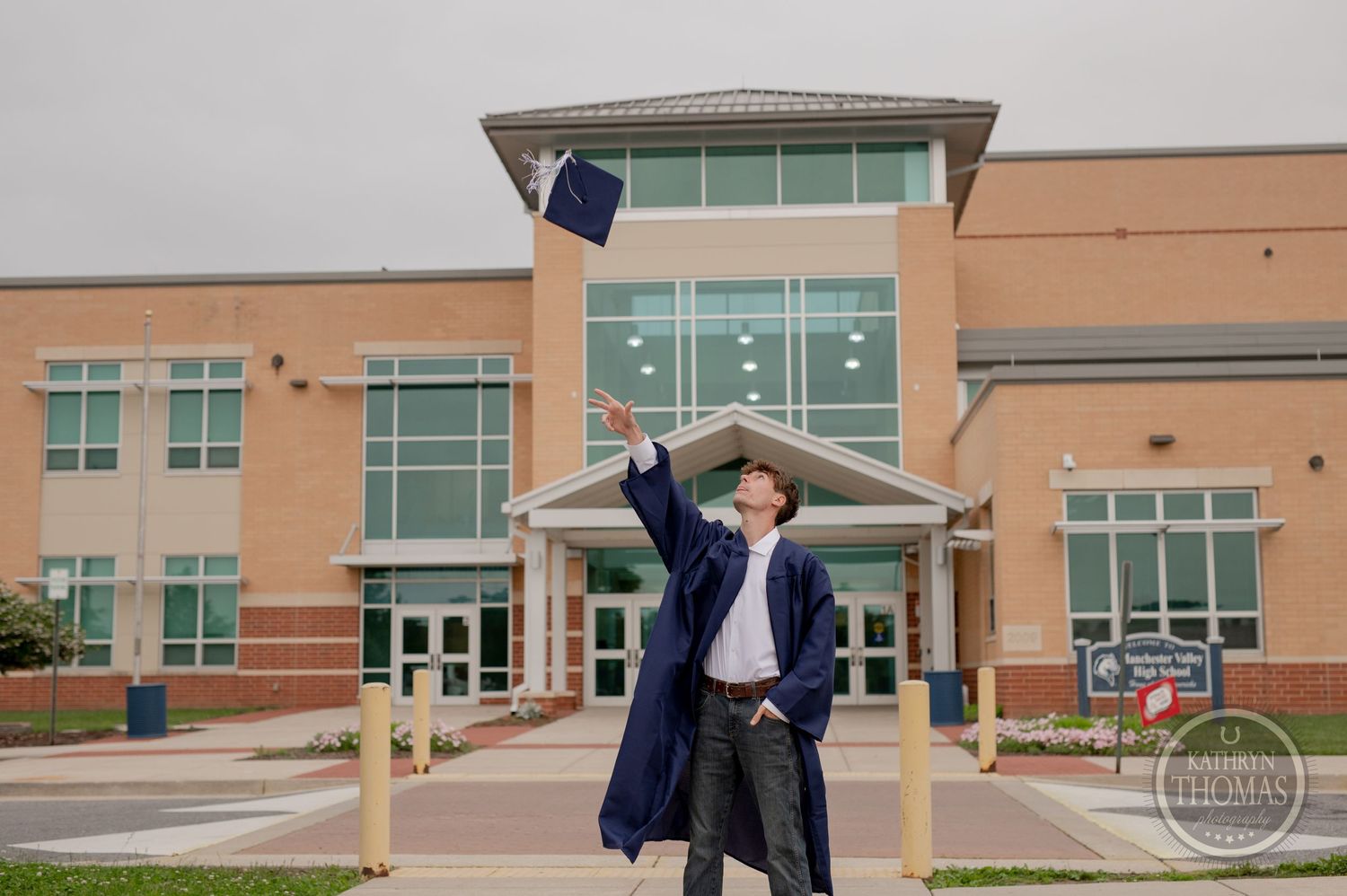 Graduate celebrates in front of modern school building entrance wearing navy cap and gown.