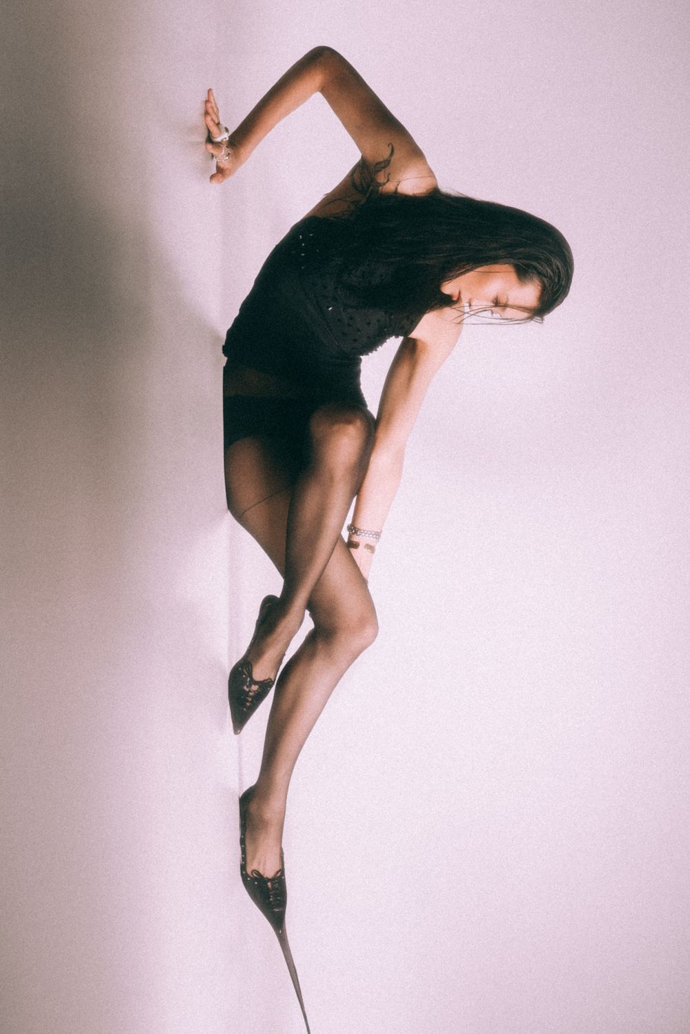 Artistic dance pose showing graceful backbend in black outfit against pink background.