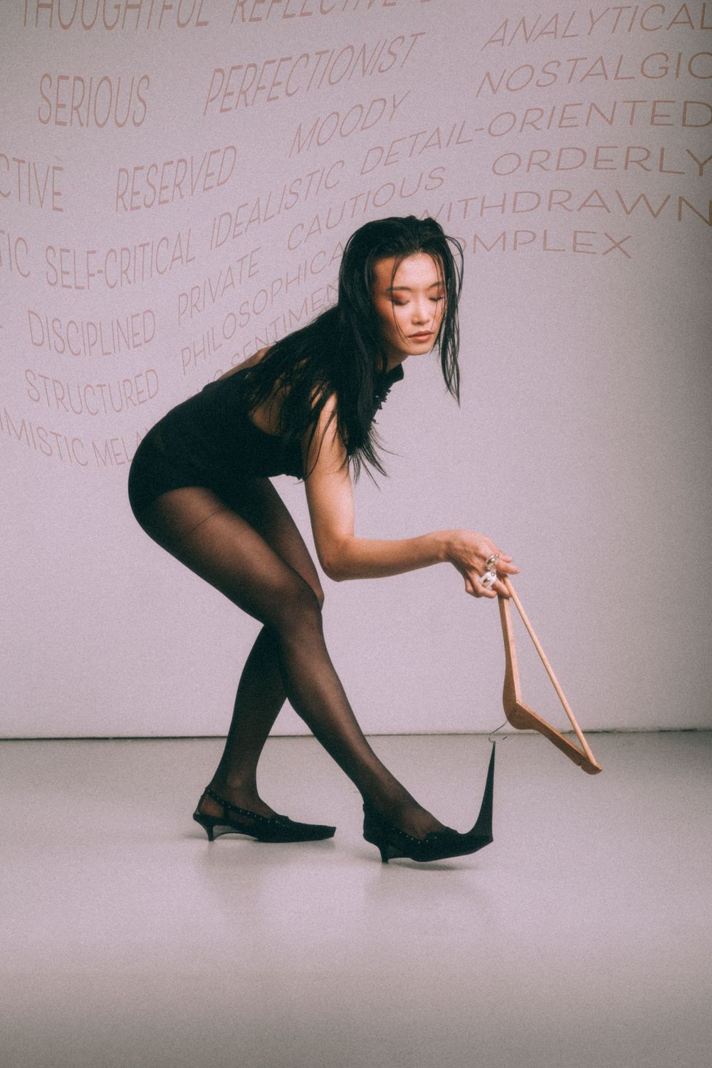 Dancer bending forward in black outfit against wall with text overlay.