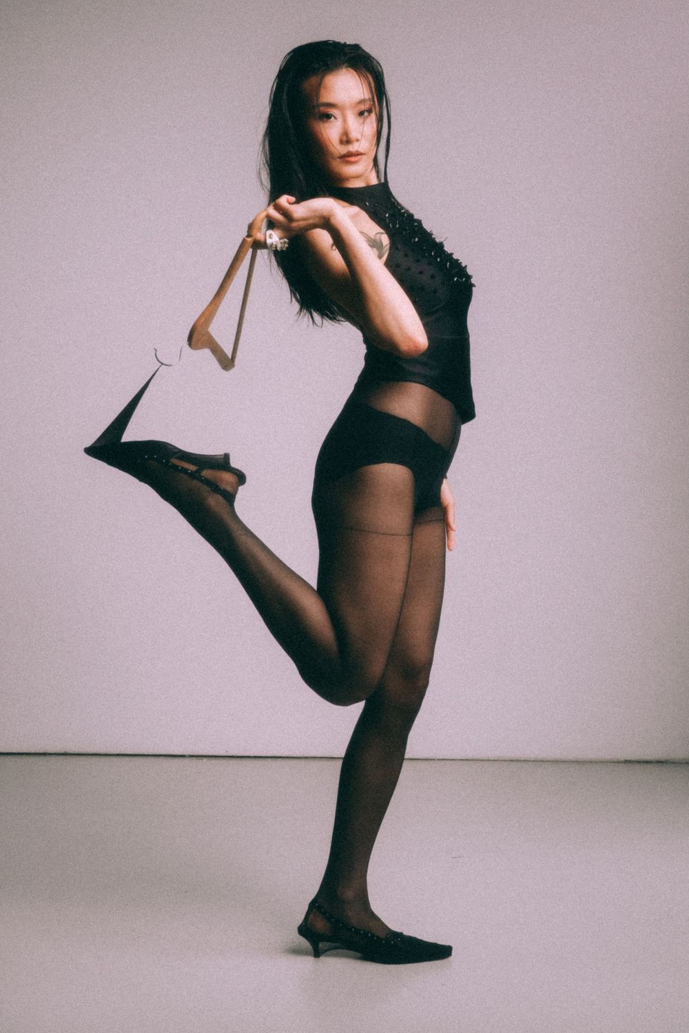 Dancer strikes graceful pose in black leotard and tights during studio photoshoot.