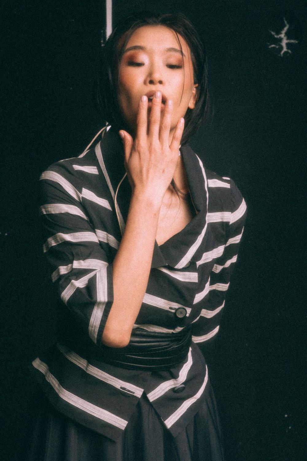 Expressive portrait in striped outfit with hand gesture against dark background.