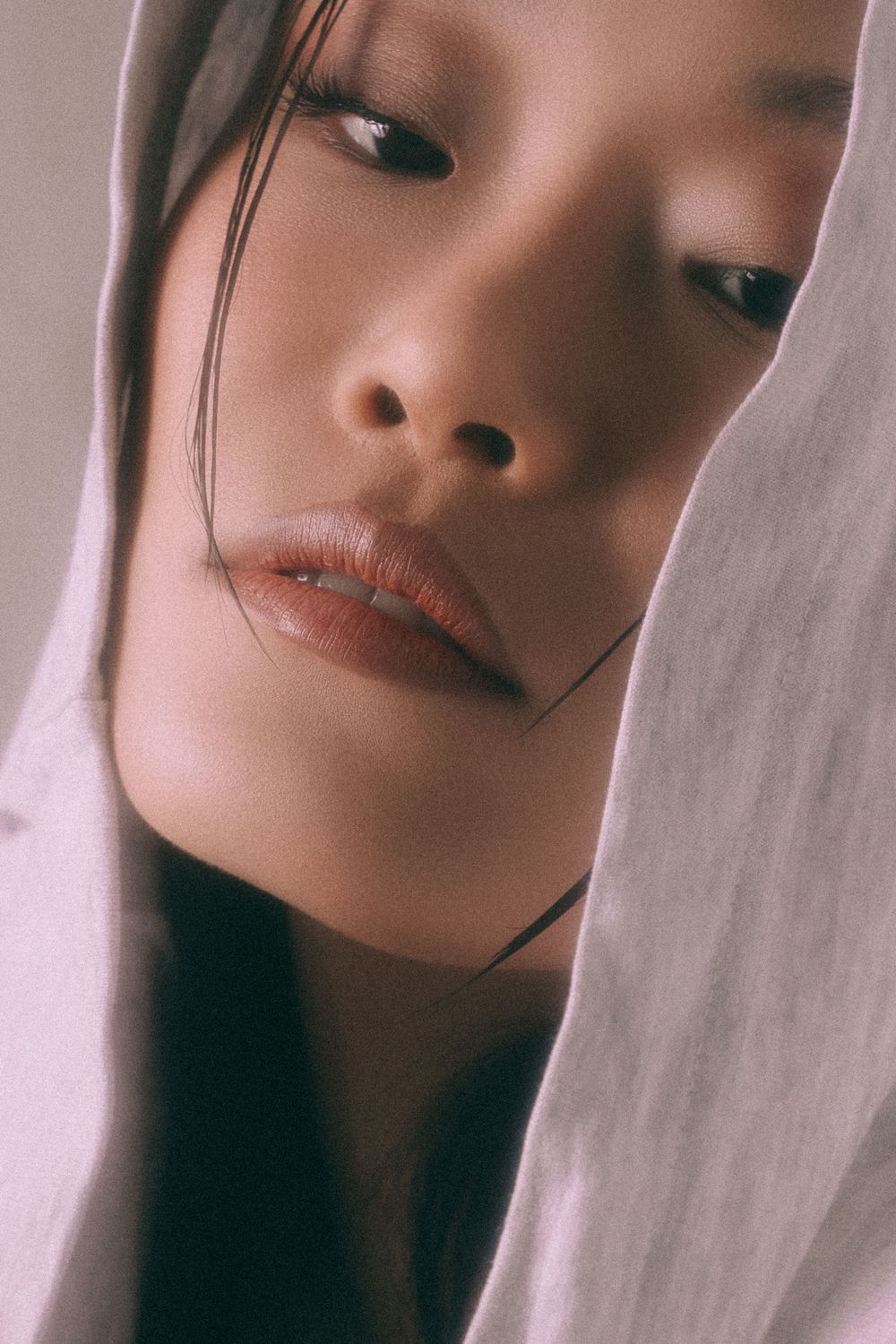 Atmospheric close-up portrait with dramatic lighting and soft fabric elements.