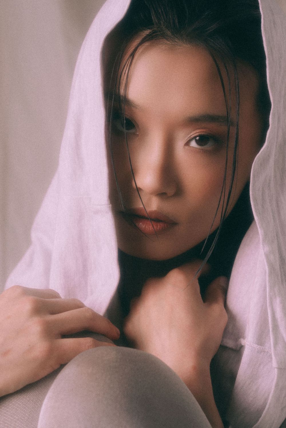 Dreamy portrait wrapped in white fabric against neutral studio backdrop.