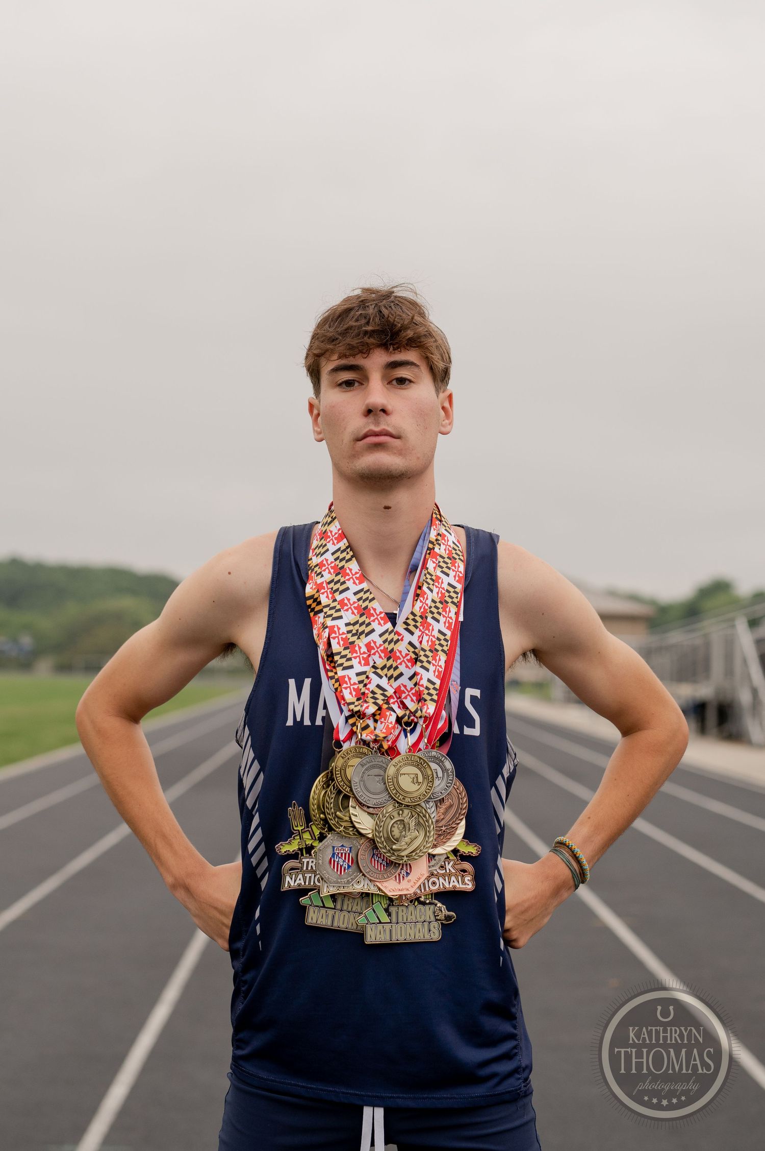An athlete stands proudly on a track wearing medals and a navy blue tank top.