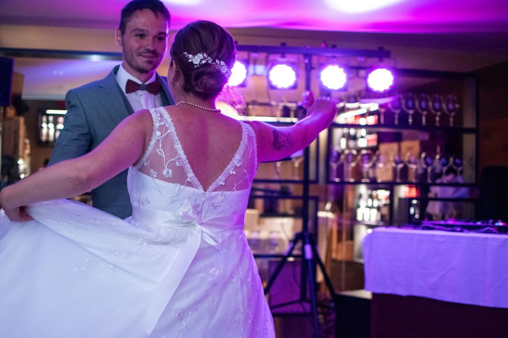 Dancing couple celebrates at wedding reception with purple lighting and bar in background.