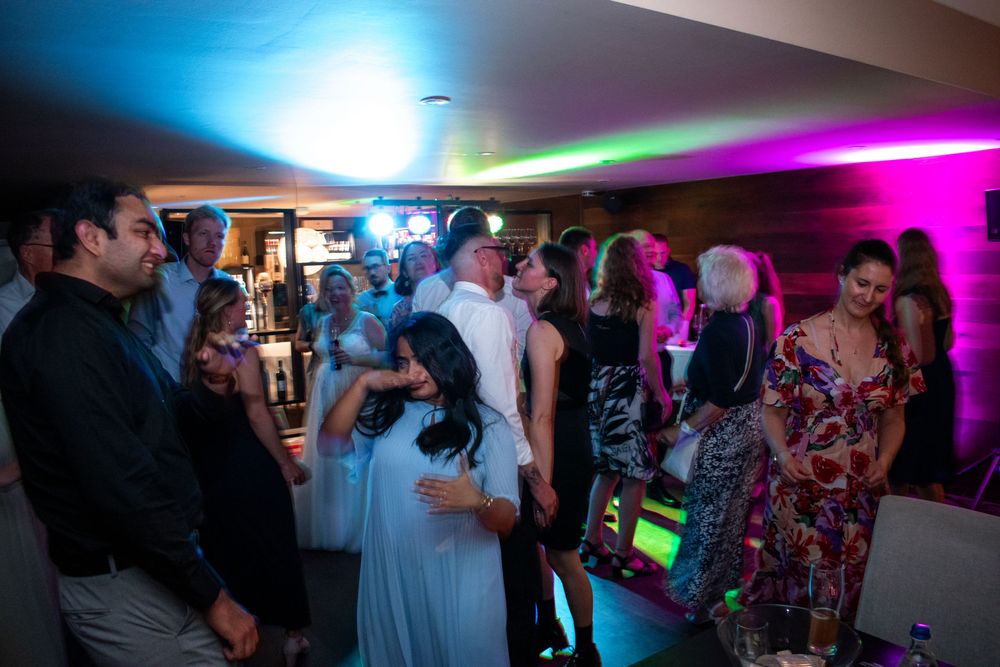 People dancing and socializing at a wedding reception with colorful lighting effects and a festive atmosphere.