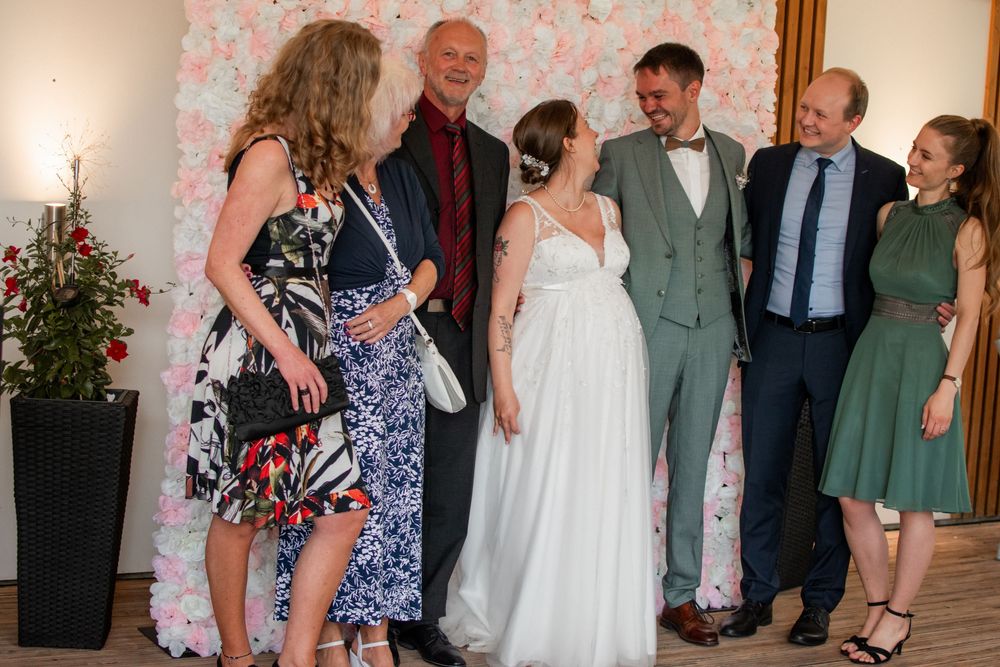 Wedding guests gathering for group photos against a floral backdrop at reception venue.