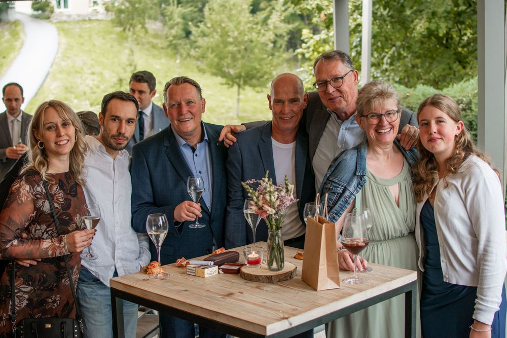 A group gathers around a table at an outdoor celebration with wine glasses and casual attire.