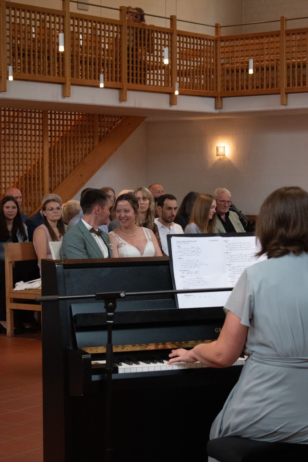 Musicians perform on multiple pianos during a musical performance in a church or concert hall.
