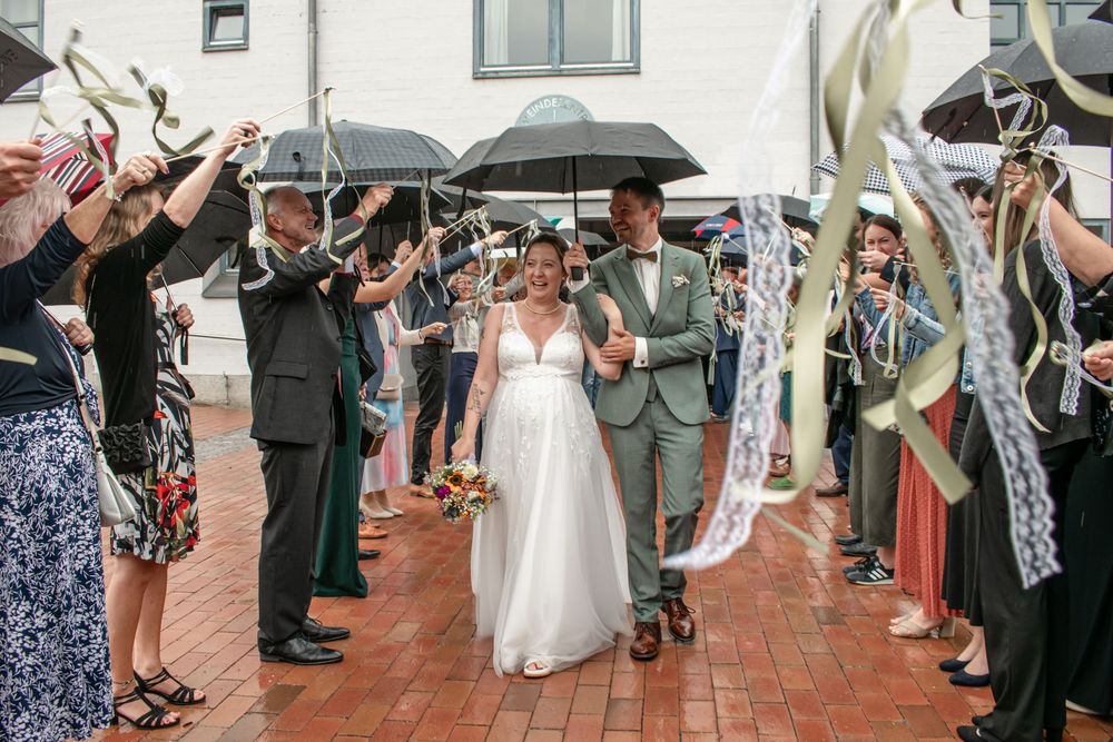 Wedding guests form a walkway holding umbrellas as newlyweds exit through a celebratory umbrella tunnel.