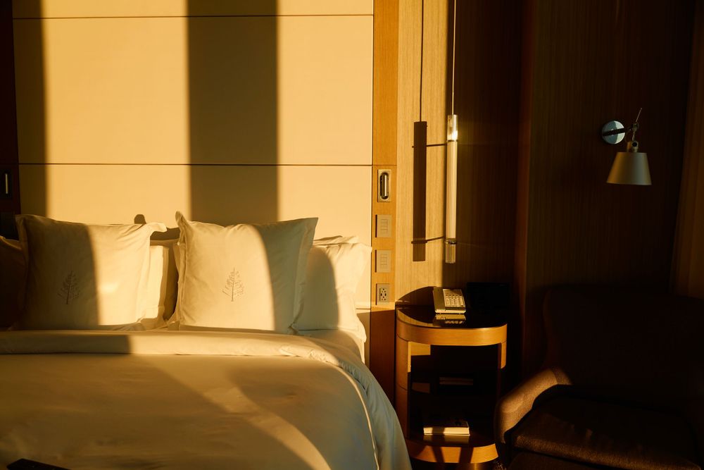Sunlit hotel bedroom with white bedding and warm golden light streaming through windows.
