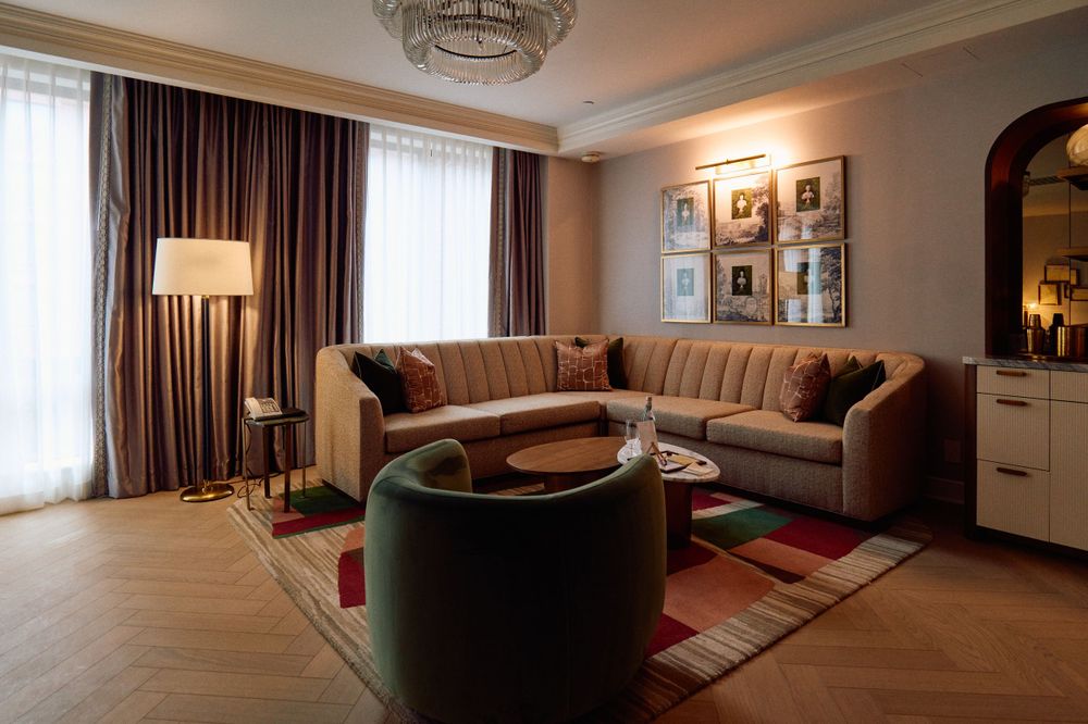 Cozy hotel living room with brown sectional sofa, round table, and framed artwork on walls.