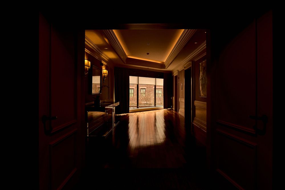 Elegant hotel corridor with warm lighting and reflective wooden floors leading to bright windows.