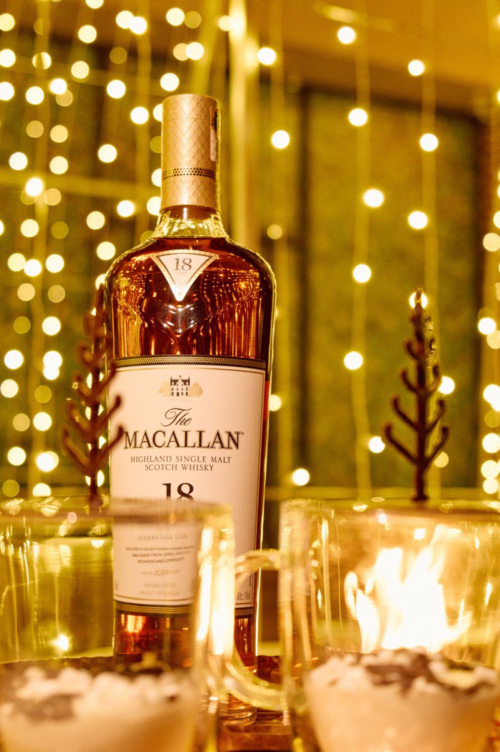 Bottle of Macallan 18 whisky displayed with bokeh lights and glassware.