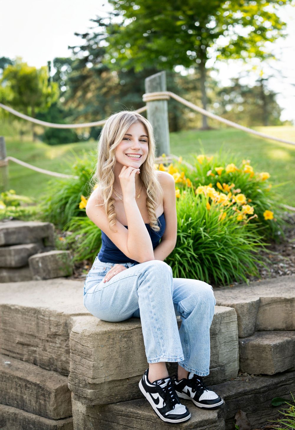 Senior portrait of person in casual attire sitting on stone steps with flowers in background.