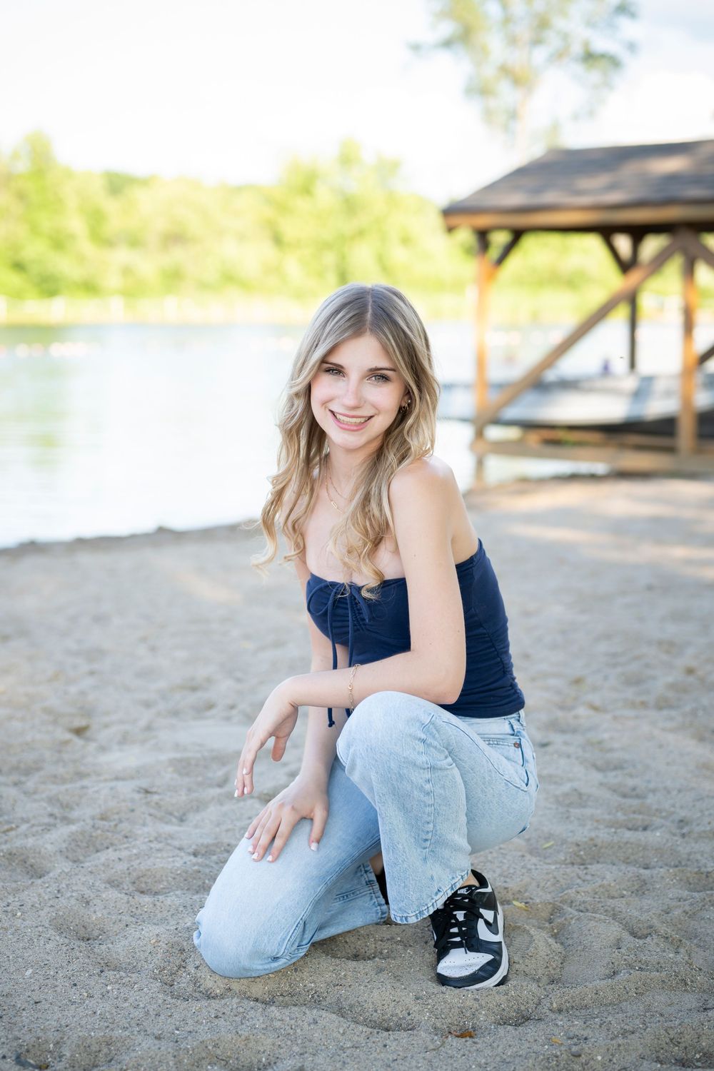 Summer portrait of person in denim and navy top posing on sandy beach near dock.
