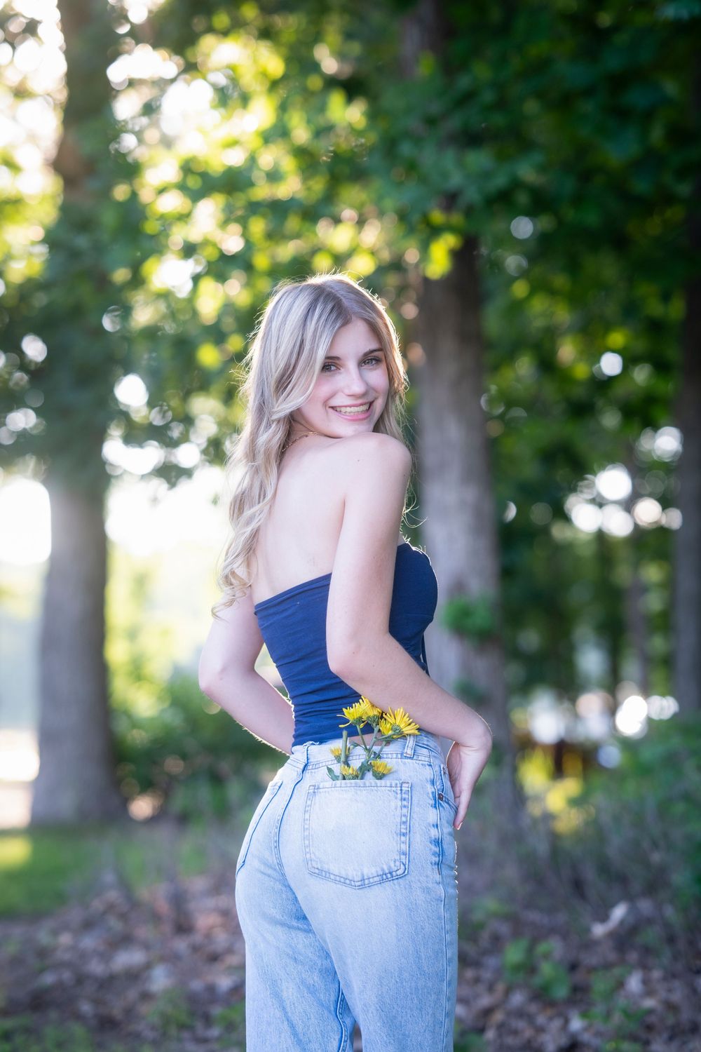 Outdoor portrait with sunlit trees showing person in casual denim and navy top.
