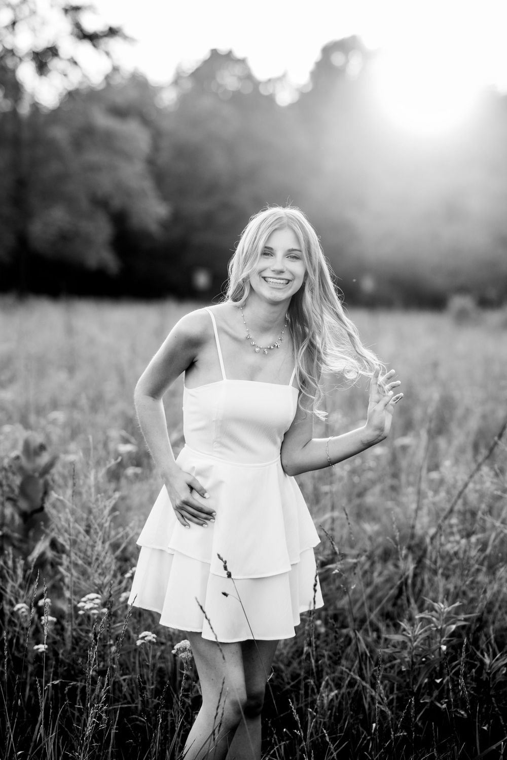 Black and white portrait of person in white dress dancing in sunlit meadow.