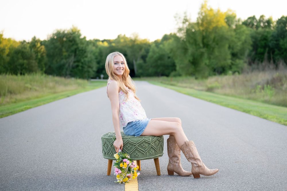 Rustic portrait sitting on vintage stool on empty road with sunflowers.
