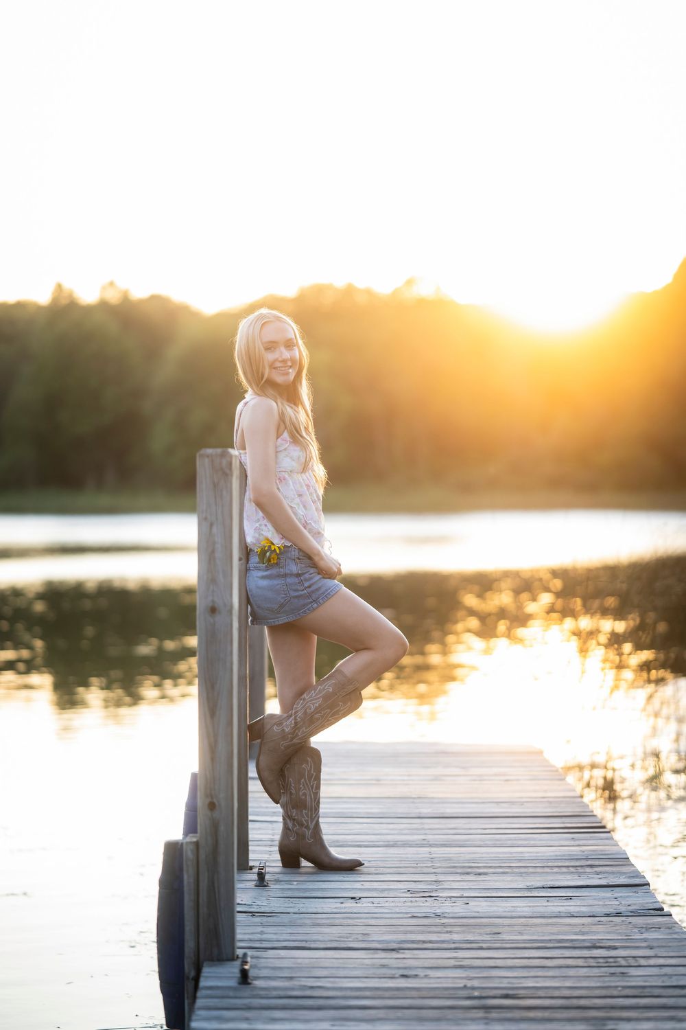 Sunset portrait on wooden dock by lake wearing cowboy boots.