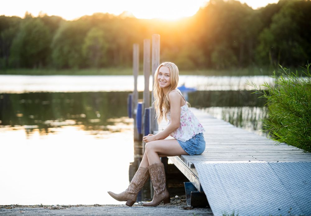 Golden hour portrait sitting on dock edge over calm water.