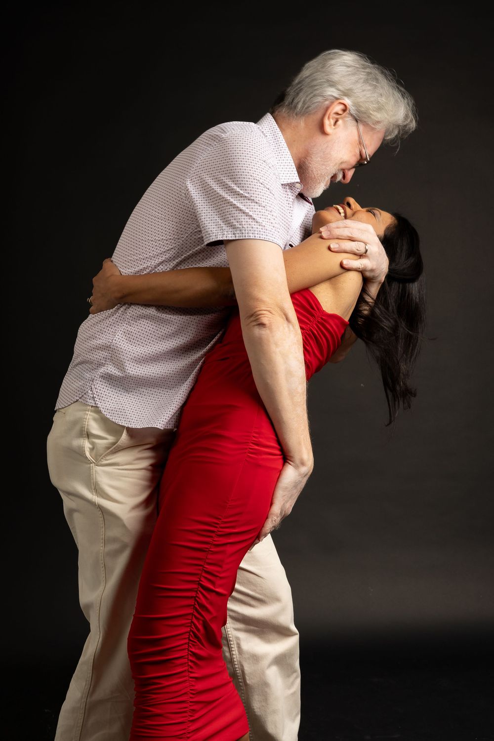 A romantic dance pose between two people, one in a fitted red dress and the other in light casual clothing.