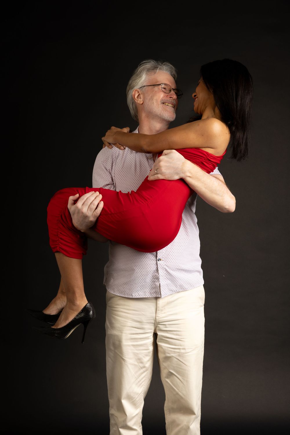 Romantic couple embracing, with woman in red dress being carried against dark backdrop.