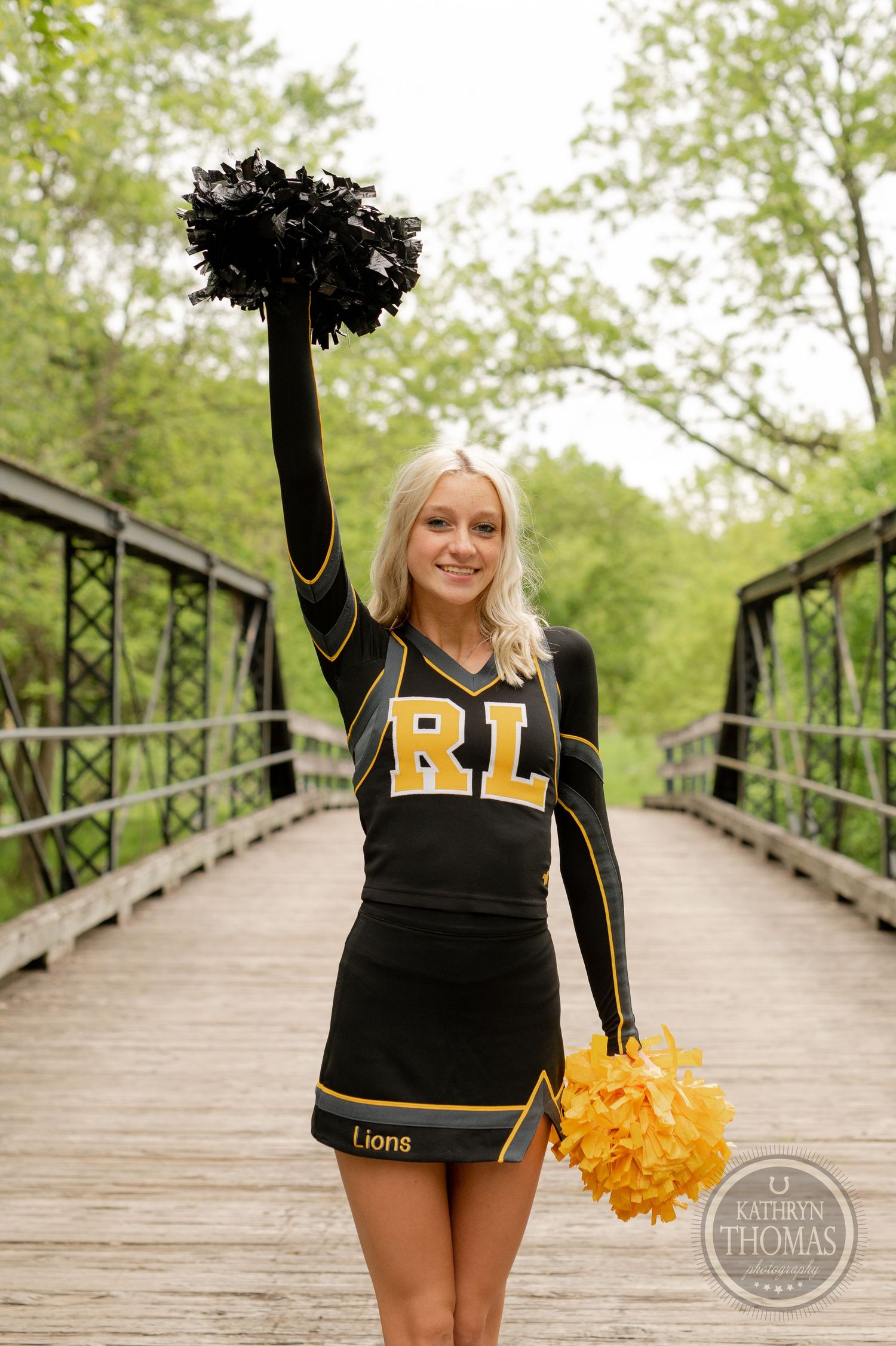 Cheerleader with raised pom pom striking pose on wooden bridge.
