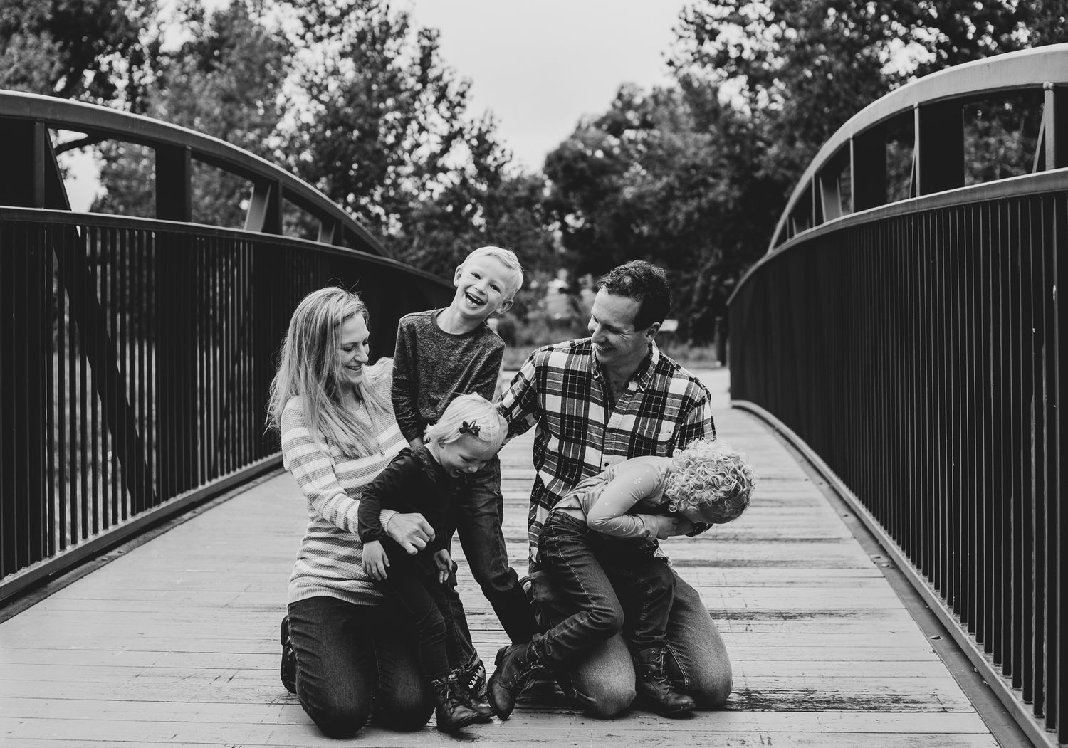 black and white picture of a family of 5 giggling and laughing for  canidi picture of them on a long bridge. happy gamily enjoying thier tim