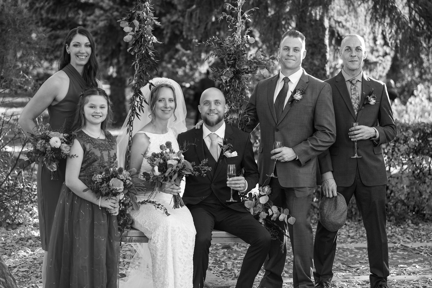 Wedding party in formal attire posed together outdoors in black and white photography.