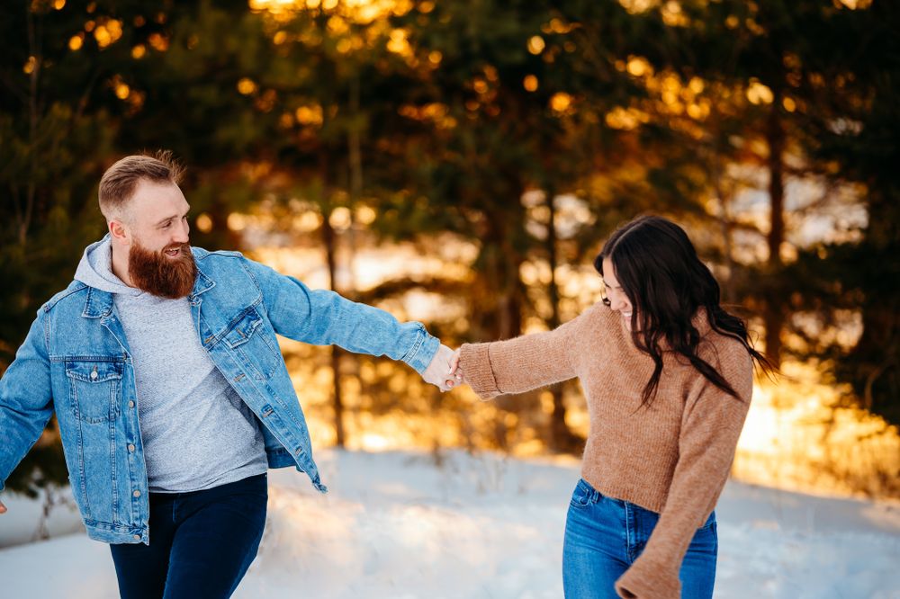 Couple playing and holding hands in snowy winter forest at sunset.