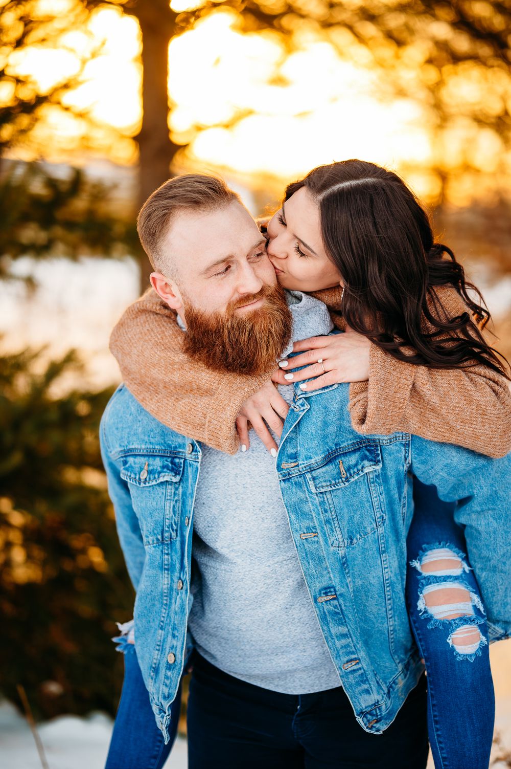 Couple in matching denim jackets share an intimate moment during sunset in a snowy landscape.