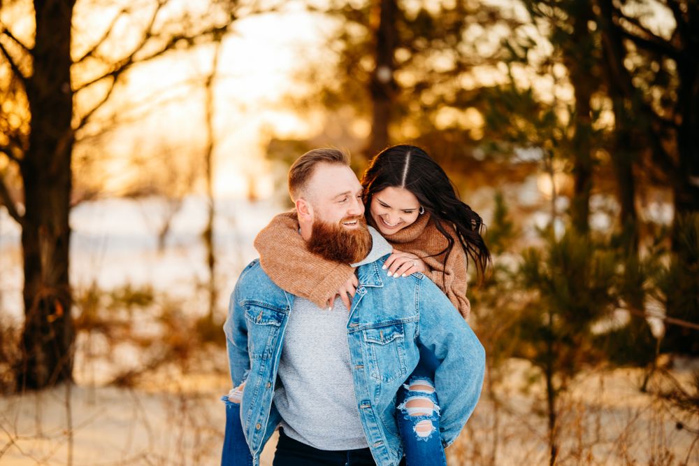 A playful winter engagement photo of a couple laughing together in warm clothing.