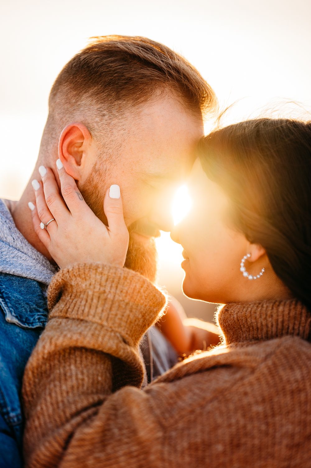 Intimate couple portrait with sunflare as they share a tender moment in winter attire.