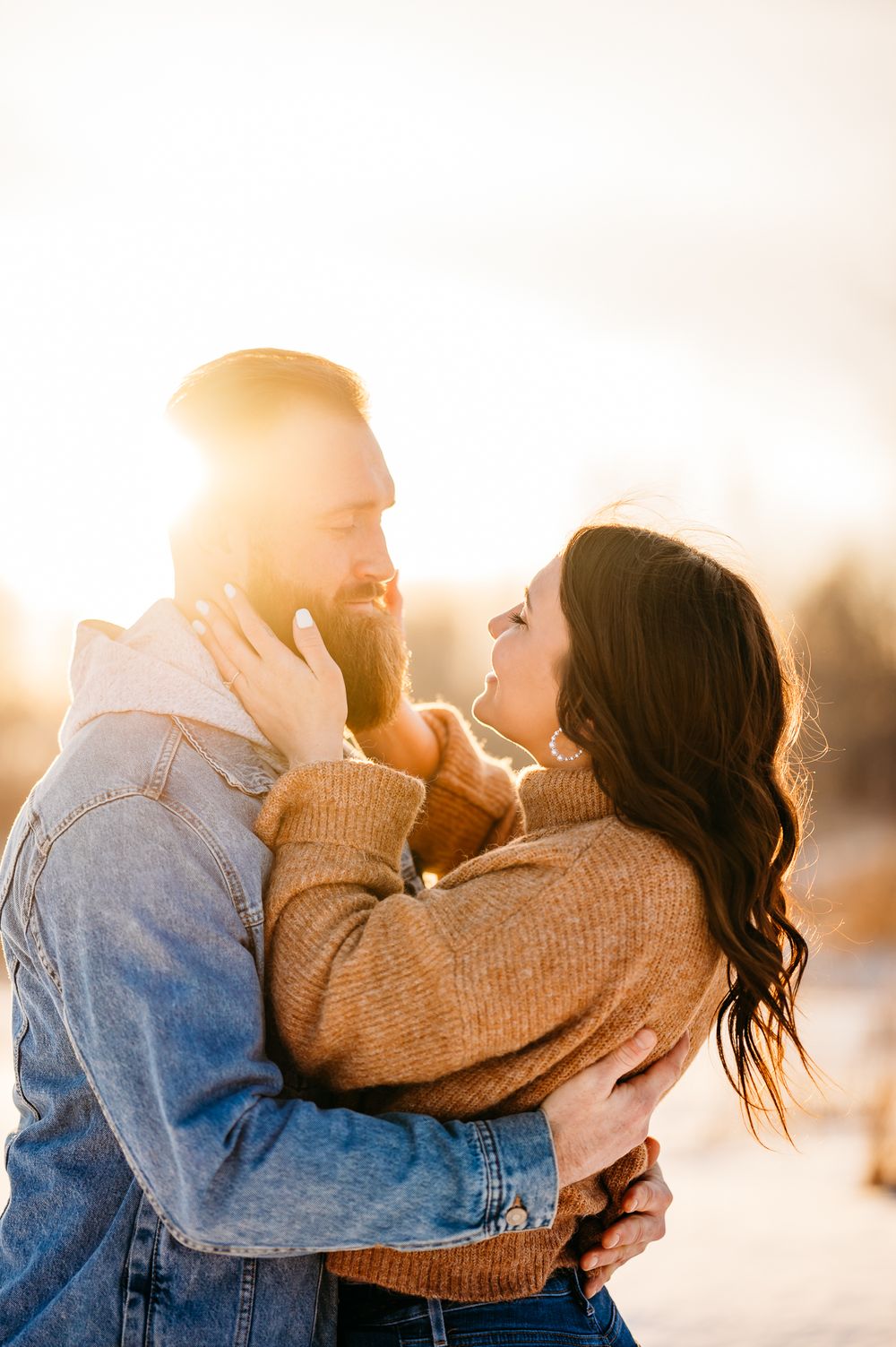 Romantic winter portrait of couple in denim and knit sweaters during golden hour.