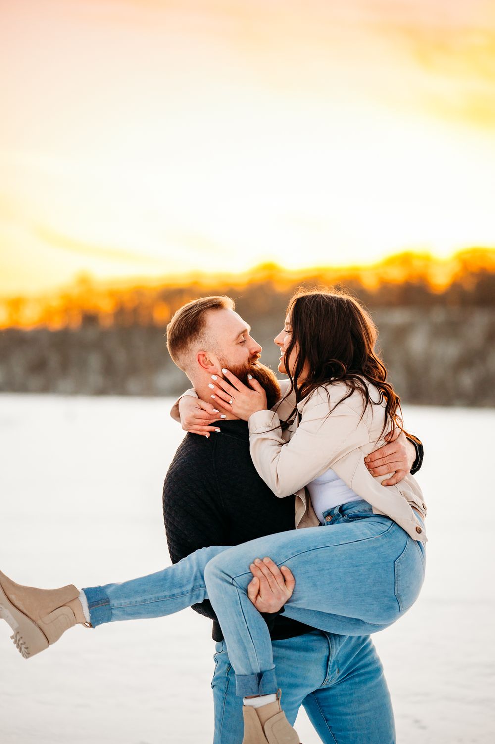 Romantic couple embracing in the snow during golden sunset with warm lighting and winter attire.