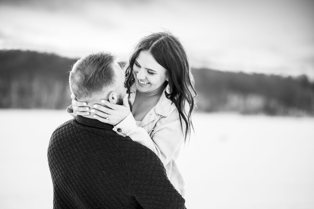 Candid black and white photo of a couple sharing a tender moment in a snowy setting.