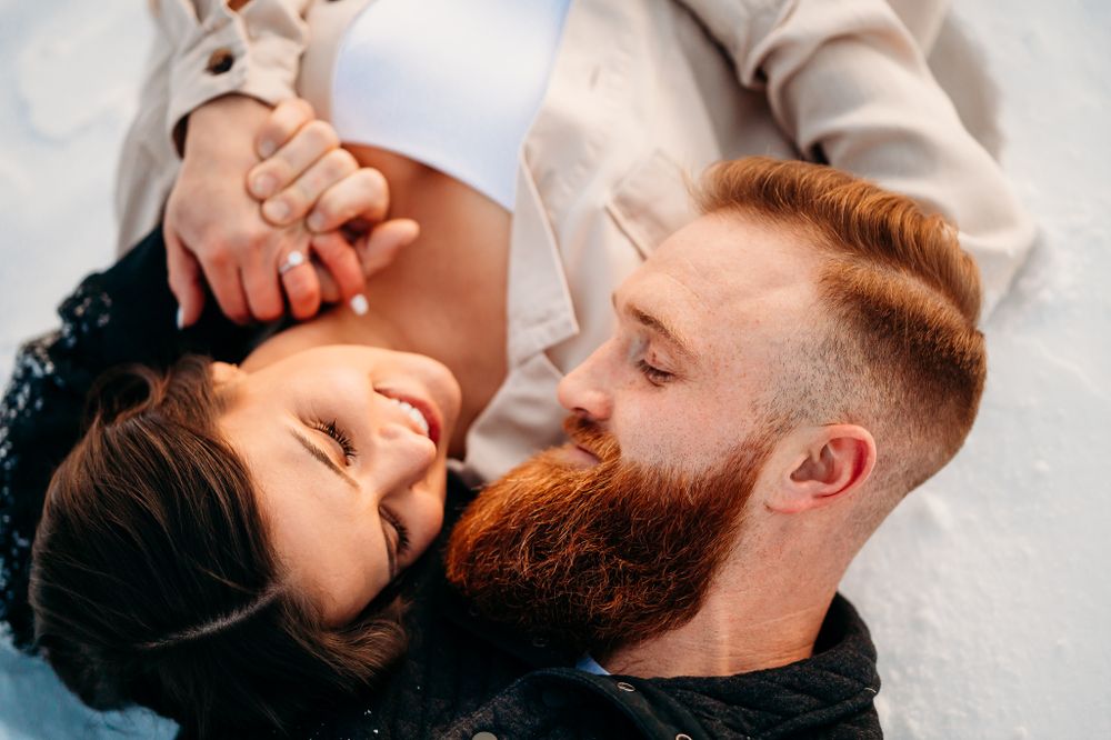 Close-up overhead shot of a couple lying in snow sharing an intimate moment.