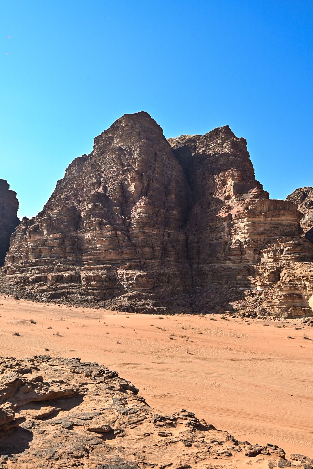 Towering sandstone cliff face rising from desert floor against bright blue sky.